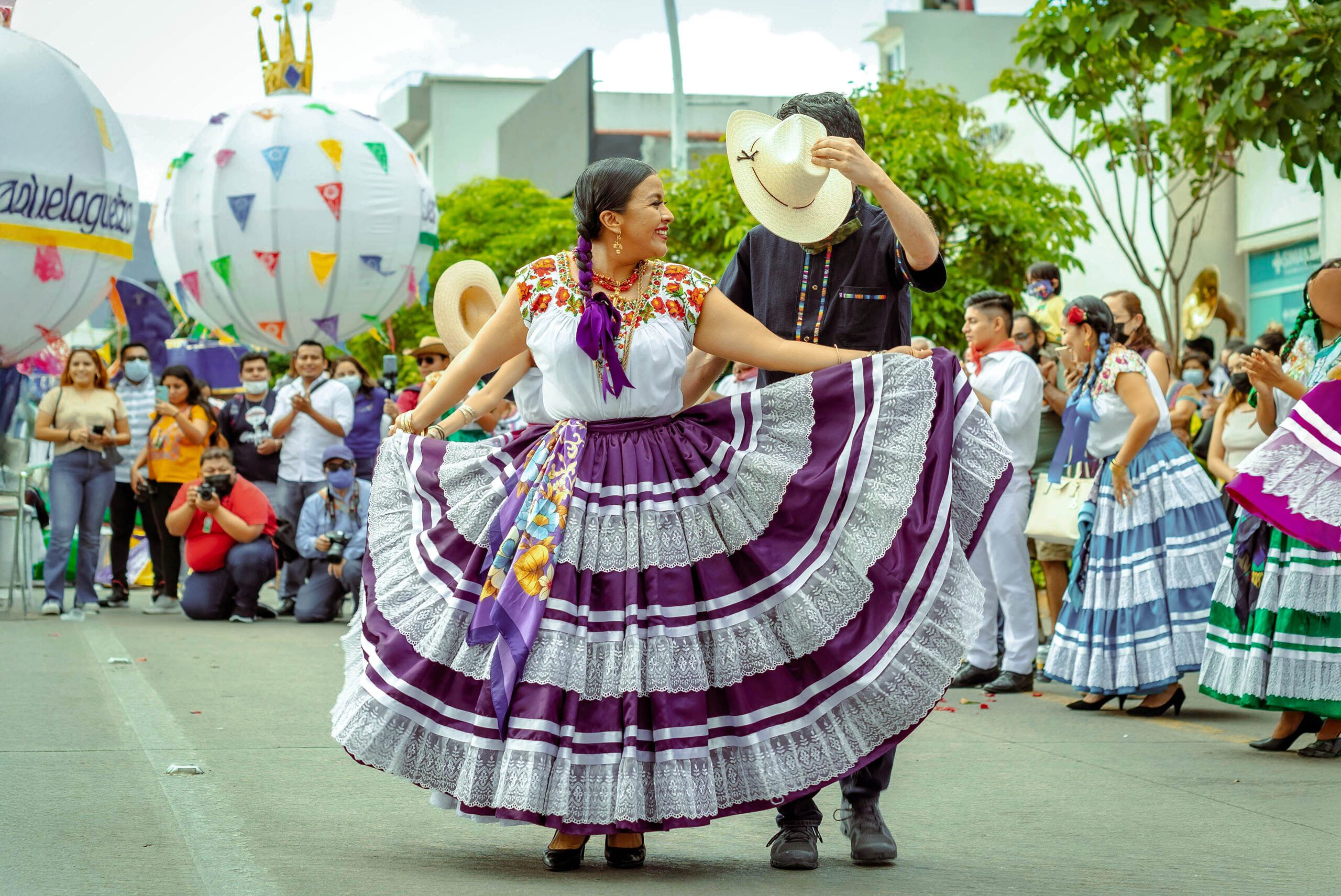 Pareja bailando en la Guelaguetza con traje tradicional de Oaxaca, durante desfile cultural.